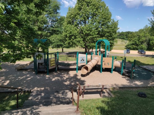 A playground with slides and tunnels surrounded by trees and grassy areas under a clear blue sky.