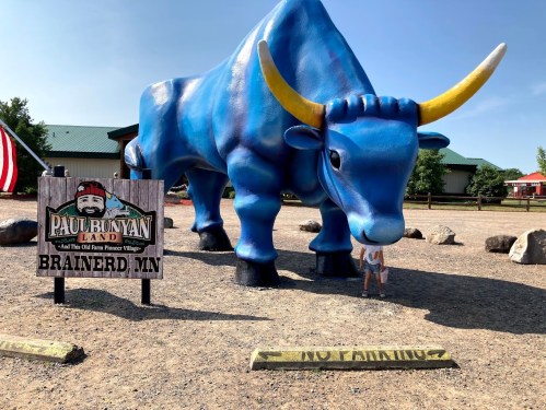 A child stands near a large blue statue of Paul Bunyan's ox at Paul Bunyan Land in Brainerd, MN.