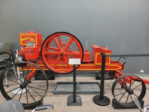 A vintage red tractor with large wheels displayed indoors, featuring yellow accents and a sign labeled "Warrior 304."