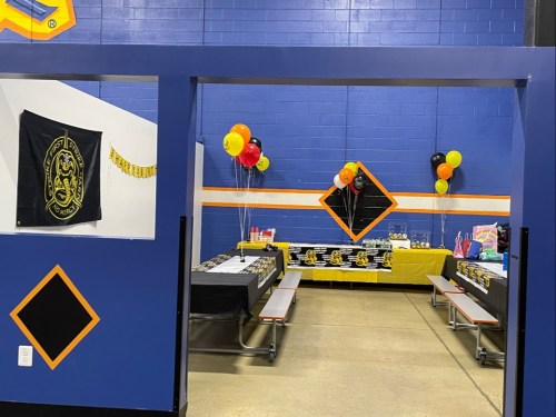 A decorated room with black and yellow balloons, tables set for a celebration, and a banner on the wall.
