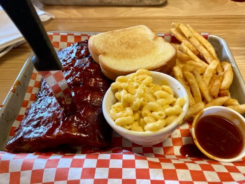 A plate with BBQ ribs, macaroni and cheese, toast, and fries, served on a checkered paper-lined tray.