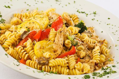 A plate of rotini pasta with chicken, vegetables, and herbs, garnished with parsley.