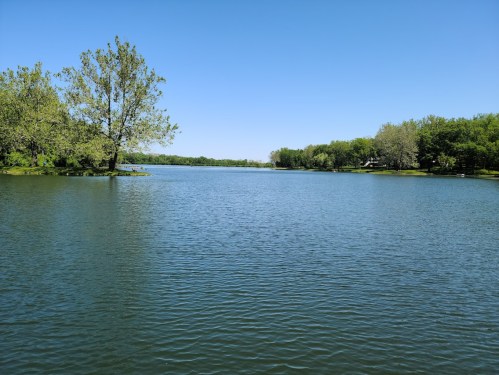 A serene lake surrounded by lush green trees under a clear blue sky.