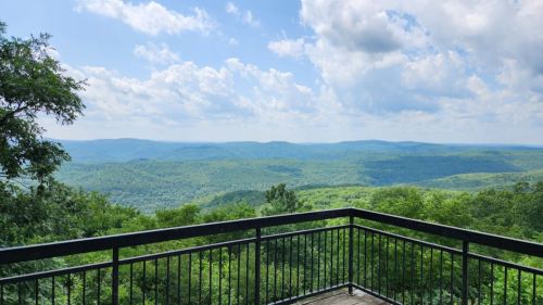 A scenic view from a balcony overlooking lush green mountains and a blue sky with fluffy clouds.