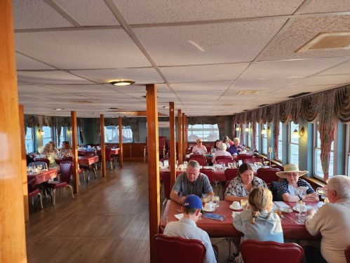 A cozy restaurant interior with diners at tables, enjoying meals in a warmly lit space with large windows.