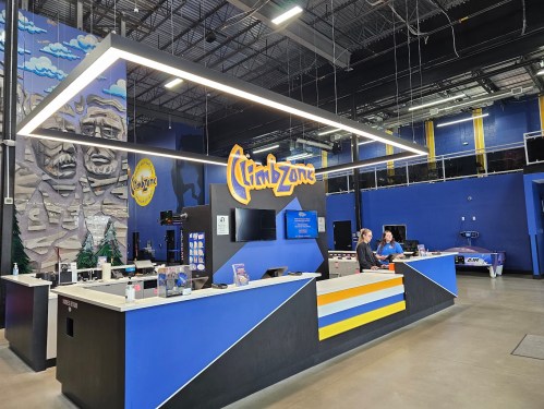 A brightly lit reception area of ClimbZone with a colorful sign, two staff members, and climbing-themed decor.