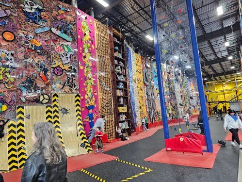 A vibrant indoor climbing gym with colorful walls, climbing holds, and various climbing structures. People are enjoying the space.