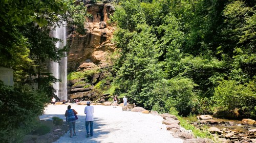 A scenic view of a waterfall surrounded by lush greenery, with people walking along a rocky path.