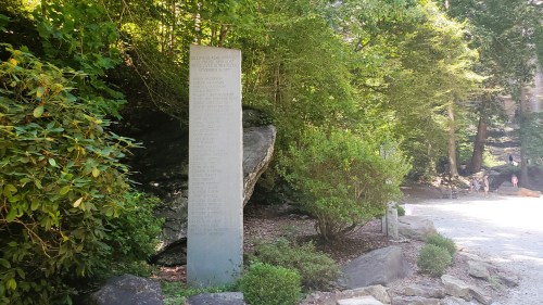 A tall stone monument surrounded by greenery, with inscriptions visible on its surface.