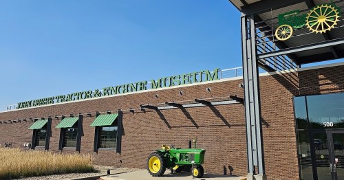 Exterior of the John Deere Tractor & Engine Museum, featuring a green tractor and a clear blue sky.