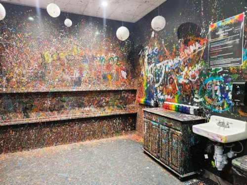 A colorful, splatter-painted room with walls and surfaces covered in vibrant paint drips and splashes.