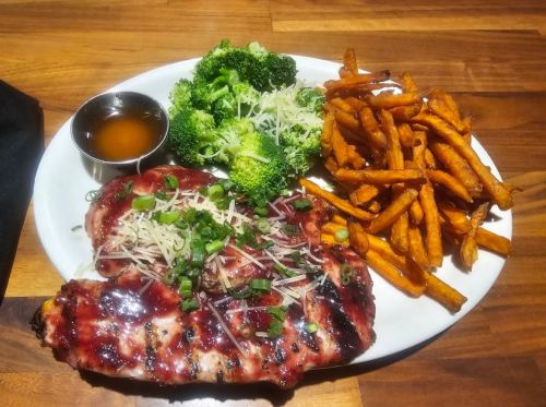 Grilled chicken with barbecue sauce, topped with green onions, served with broccoli and sweet potato fries.