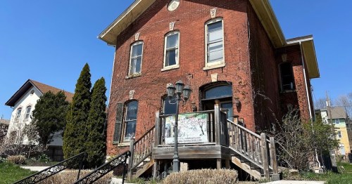 Historic red brick building with a wooden staircase, surrounded by greenery and a clear blue sky.