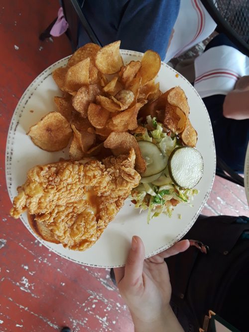 A plate with fried chicken sandwich, potato chips, and a side of salad with cucumber slices.