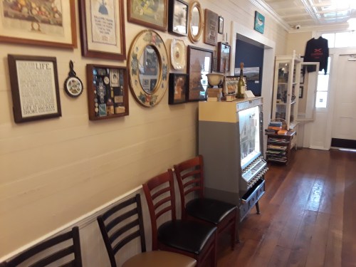A hallway with wooden floors, featuring a vintage jukebox and a wall adorned with various framed pictures and memorabilia.