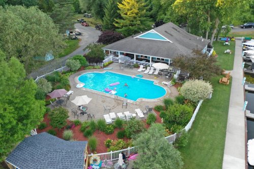 Aerial view of a pool area with lounge chairs, umbrellas, and a house surrounded by greenery and trees.