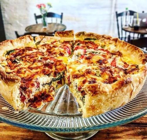 A freshly baked pizza with a golden crust, topped with cheese, tomatoes, and greens, on a glass serving platter.