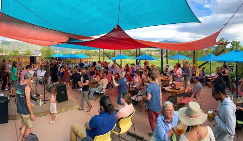 A lively outdoor gathering with a crowd enjoying music under colorful canopies and umbrellas.