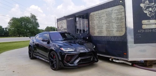 A sleek black sports car parked next to a food truck with a metallic exterior and menu displayed on the side.