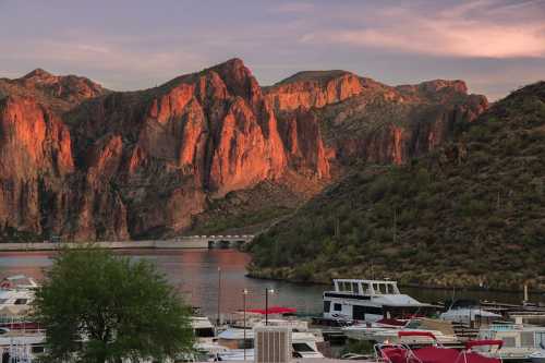 Sunset over rocky cliffs reflecting warm colors, with boats docked in a serene marina by the water.