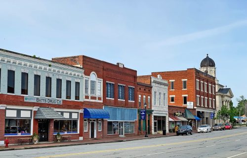 A charming small-town street featuring historic brick buildings and shops under a clear blue sky.