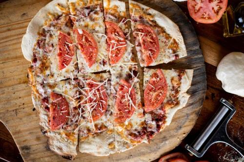 A freshly baked pizza topped with sliced tomatoes and cheese, cut into six pieces on a wooden board.