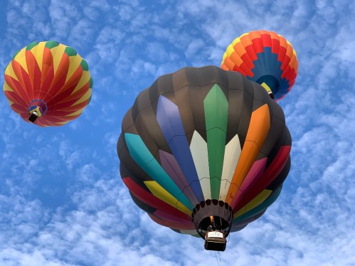 Three colorful hot air balloons float against a blue sky with fluffy clouds.