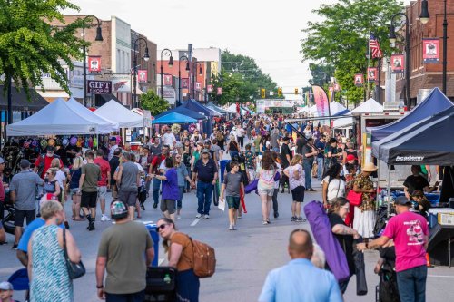 A bustling street fair with crowds, vendor tents, and colorful displays under a clear sky.