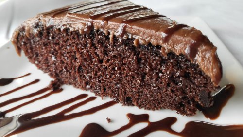 A slice of rich chocolate cake with creamy frosting and chocolate drizzle on a white plate.