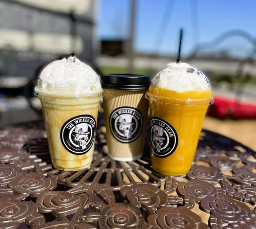 Three coffee drinks on a decorative table: a frosty beverage with whipped cream, a hot coffee cup, and a smoothie.
