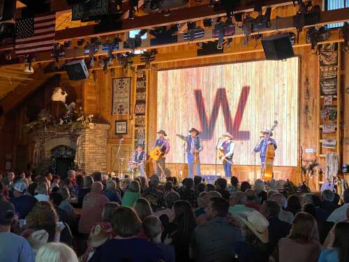 A country band performs on stage in a rustic venue, with a large audience enjoying the show.