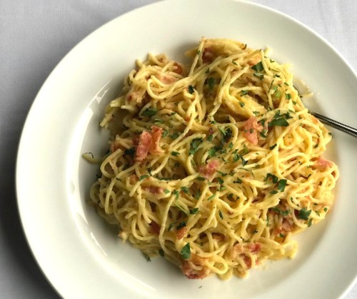 A plate of spaghetti carbonara topped with parsley, served on a white dish.
