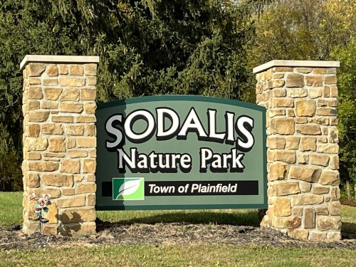 Sign for Sodalis Nature Park in Plainfield, featuring stone pillars and greenery in the background.
