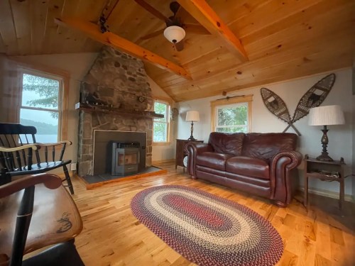 Cozy living room with a stone fireplace, leather sofa, wooden beams, and decorative snowshoes on the wall.