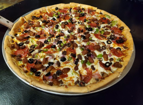 A large pizza topped with pepperoni, sausage, olives, green peppers, and cheese on a golden crust.
