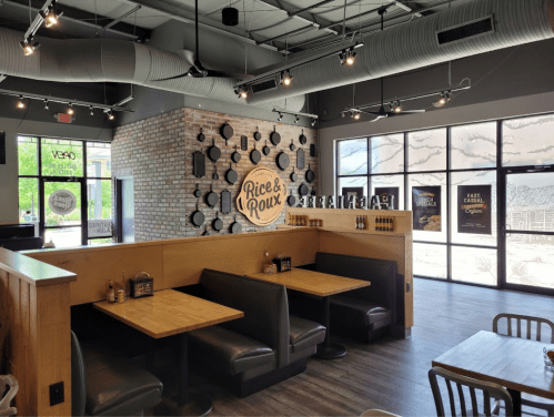 Interior of a restaurant featuring wooden booths, a brick wall, and large windows with decorative designs.