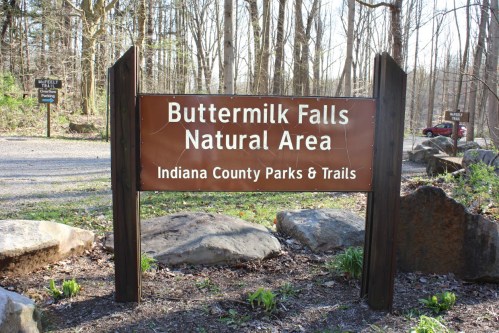 Sign for Buttermilk Falls Natural Area, Indiana County Parks & Trails, surrounded by trees and rocks.
