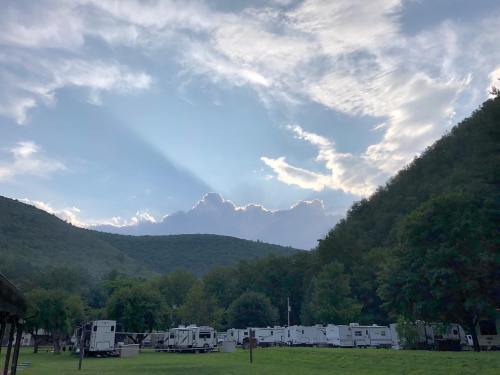 A scenic view of mountains under a cloudy sky, with RVs parked in a green field below.