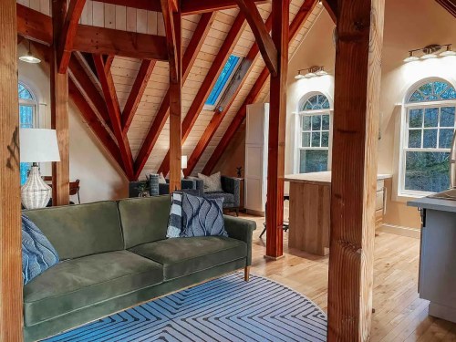 Cozy interior of a modern cabin featuring a green sofa, wooden beams, and large windows.