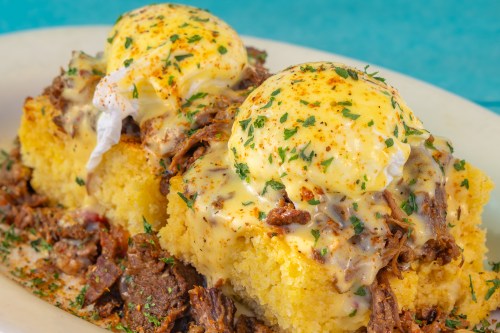 Two poached eggs on cornbread topped with shredded beef and creamy sauce, garnished with herbs and spices.