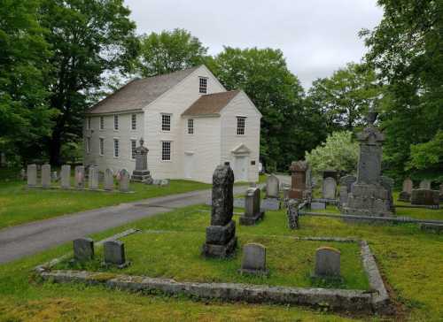 A historic building beside a cemetery, featuring various gravestones and surrounded by lush green trees.