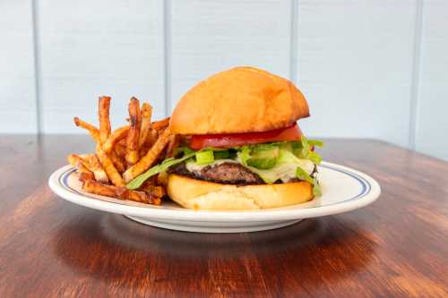 A juicy hamburger with lettuce, tomato, and fries on a plate, set against a light blue background.