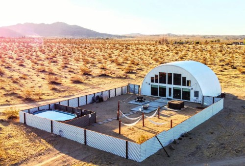 A modern dome-shaped structure surrounded by desert landscape, featuring a pool and outdoor seating area.