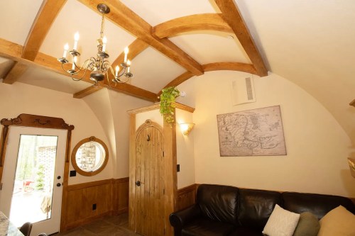 Cozy interior with wooden beams, a chandelier, and a round mirror, featuring a leather couch and a decorative door.
