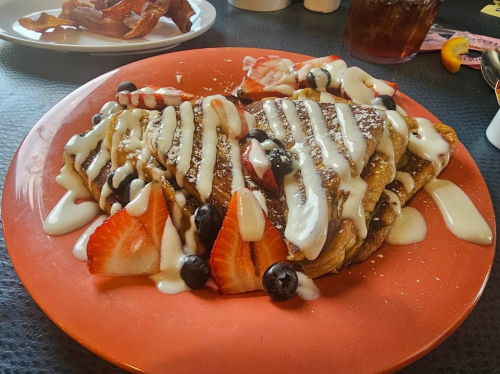 A plate of French toast topped with strawberries, blueberries, and drizzled with cream sauce.