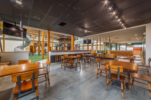 A spacious, modern dining area with wooden tables, chairs, and a play area in the background. Bright and inviting atmosphere.
