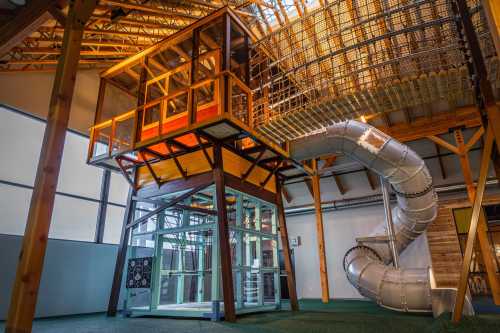 A colorful indoor play structure with a slide, featuring multiple levels and a transparent elevator.