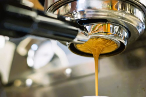 Close-up of espresso being extracted from a coffee machine, with rich brown liquid flowing into a cup.