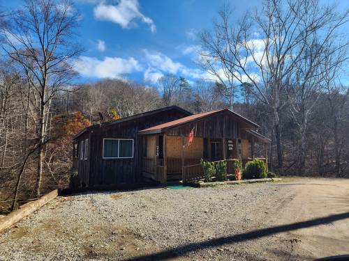A rustic wooden cabin surrounded by trees, with a gravel driveway and blue sky in the background.