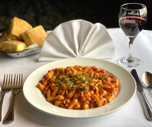 A plate of pasta in tomato sauce garnished with herbs, accompanied by bread rolls and a glass of red wine.